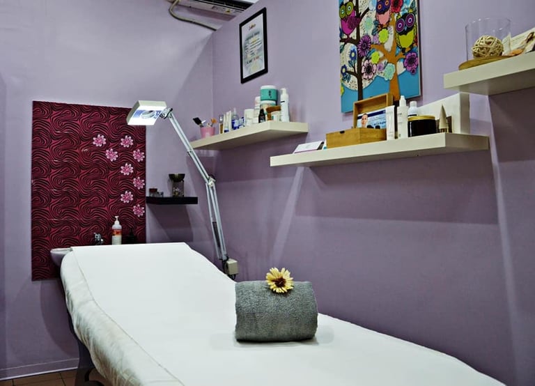 Professional treatment room with white massage bed, purple walls, wall-mounted shelves with supplies, and burgundy decorative panel