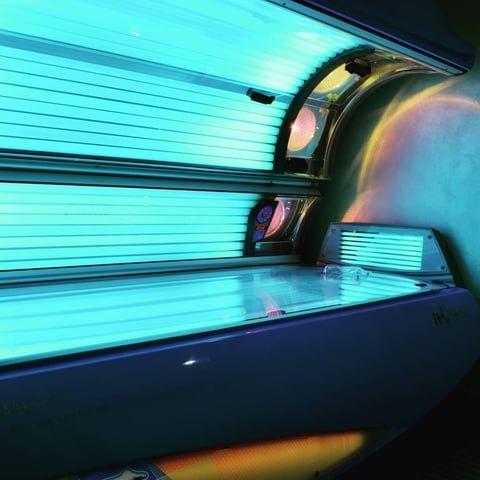 Interior view of a tanning bed with glowing cyan fluorescent tubes and reflective bulbs